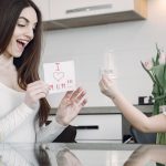 A mother and daughter sharing a joyful moment with flowers and a card in a kitchen.
