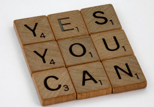 Wooden Scrabble tiles on white surface spelling 'Yes You Can,' promoting positivity and motivation.